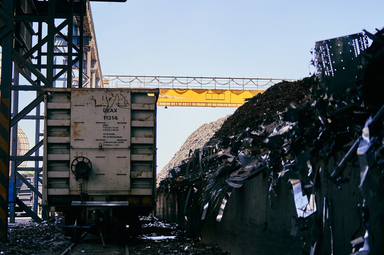 Train car at an industrial scrap metal yard with conveyor belt and metal piles.