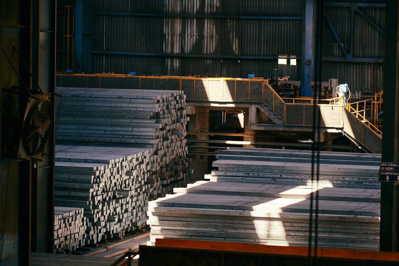 Interior view of a large industrial warehouse with stacked metal sheets and beams.